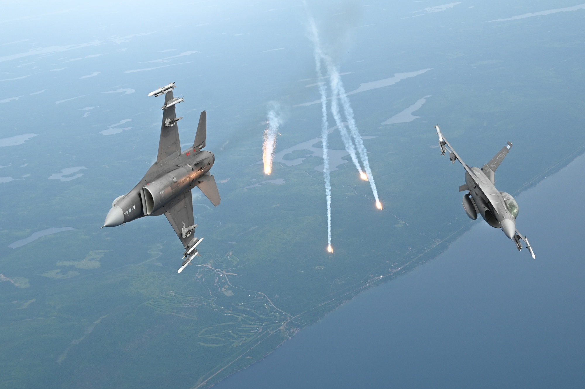 Aircraft releasing countermeasure flares over a blue-gray landscape
