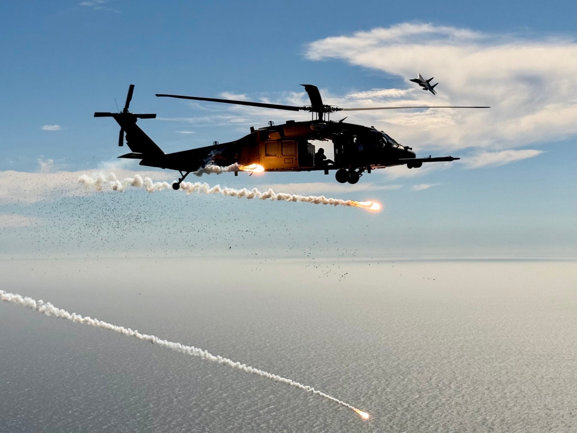 HH-60G helicopter releasing countermeasure flares over water during a test flight
